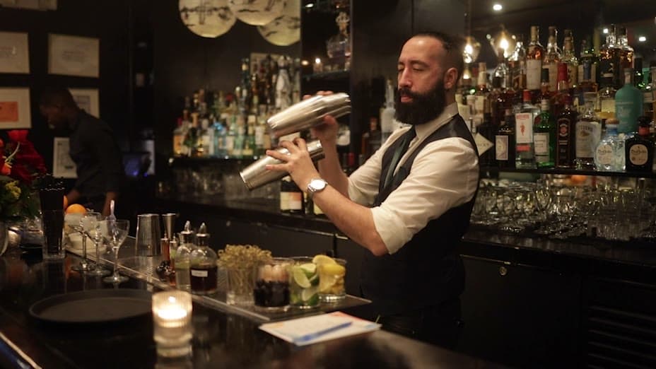 A bartender shaking a cocktail behind a candlelit bar at an evening event