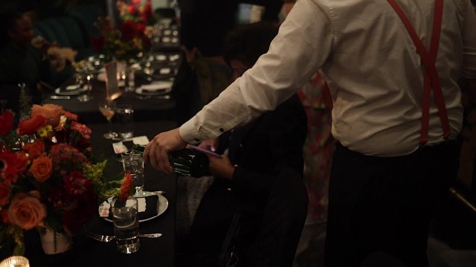A server pouring wine beside a table centerpiece of red and orange florals